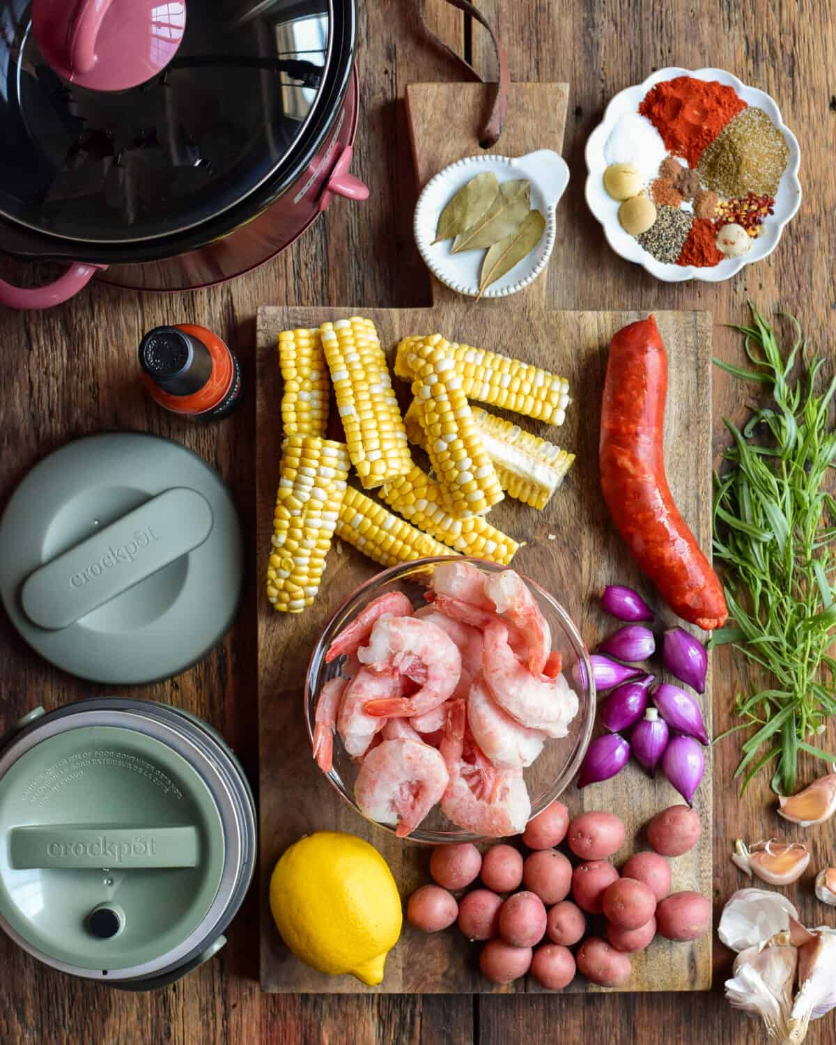 Ingredients for a shrimp boil are laid out beside two crockpots.