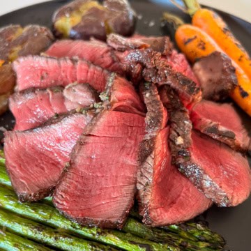 A perfectly cooked filet Mignon slices and fanned on a plate with asparagus, carrots and potatoes.