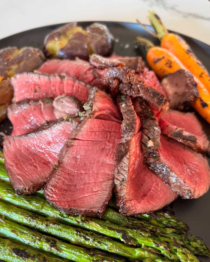 A perfectly cooked filet Mignon slices and fanned on a plate with asparagus, carrots and potatoes.