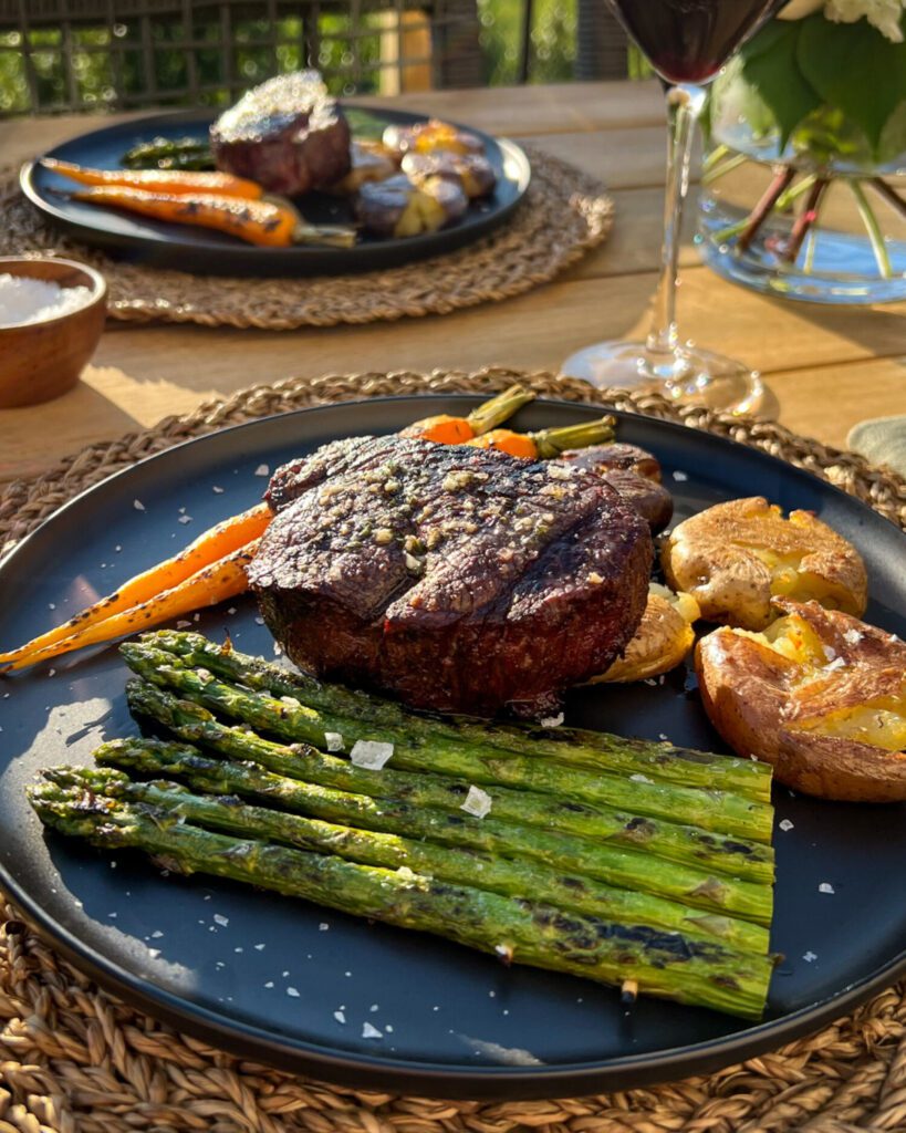 A finished reverse sear filet mignon on a plate with asparagus, carrots and potatoes.
