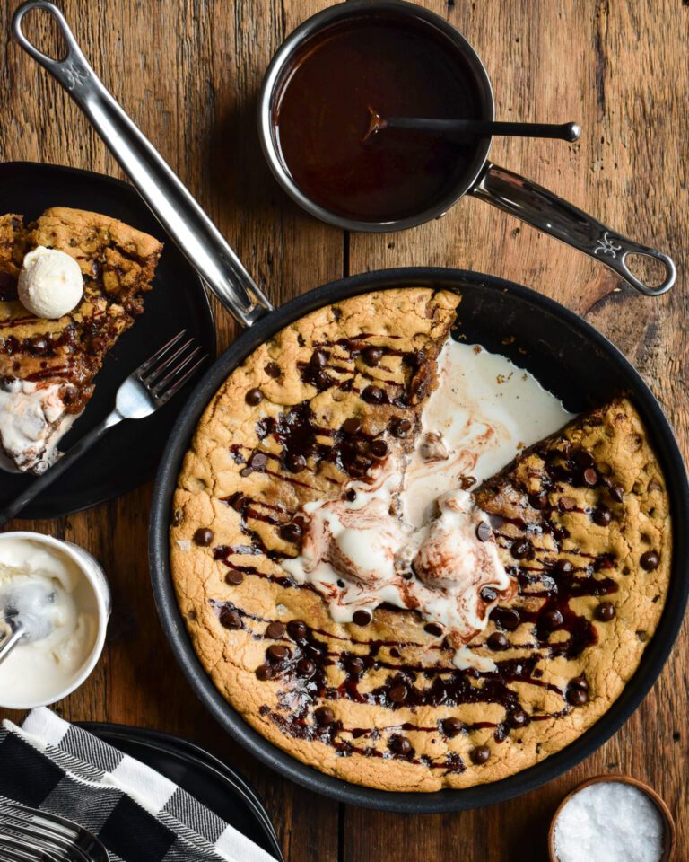 A top down image of a skillet chocolate chip cookie with a slice taken out and melted ice cream in the centre.