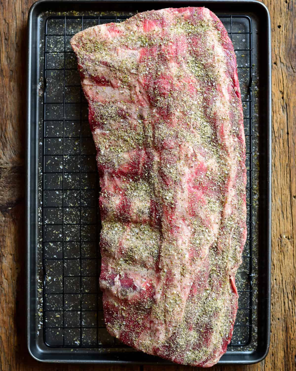 A large rack of beef ribs that has just been dry rubbed with spices.