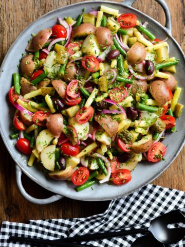 A top down image of a potato, bean, tomato and onion salad in a light blue round platter with handles.