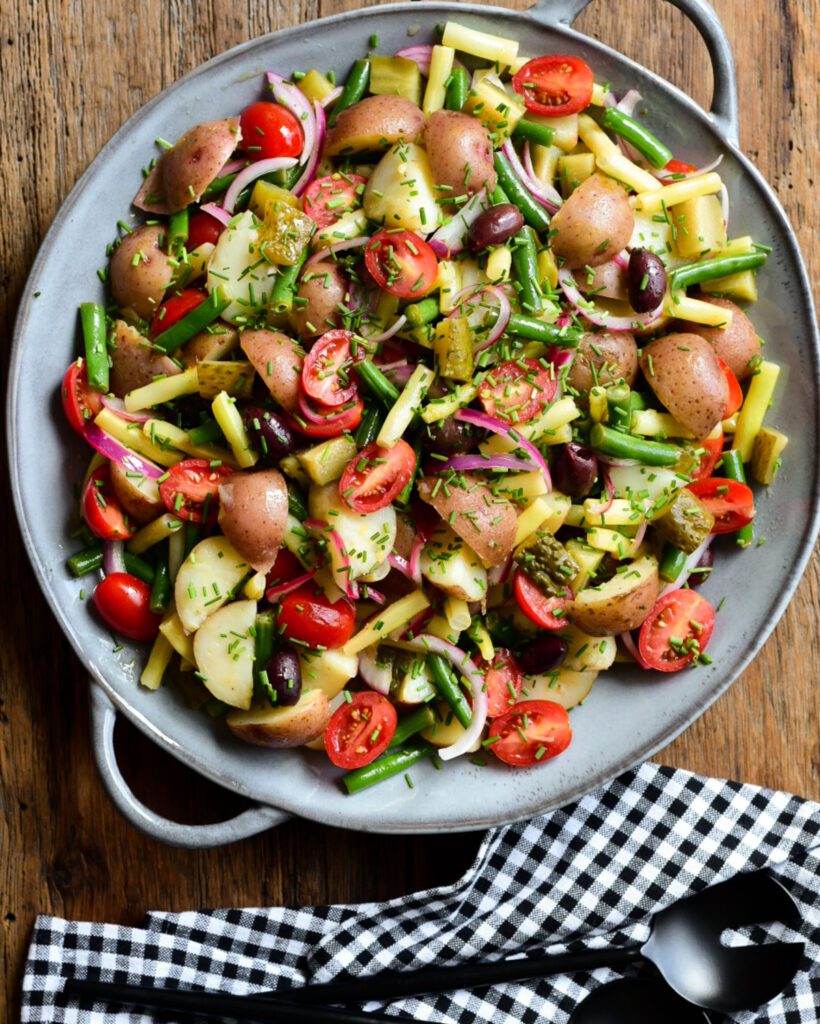 A top down image of a potato, bean, tomato and onion salad in a light blue round platter with handles. 