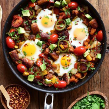 A top down of a skillet hash with four sunny side up eggs and loaded with potatoes and veggies.
