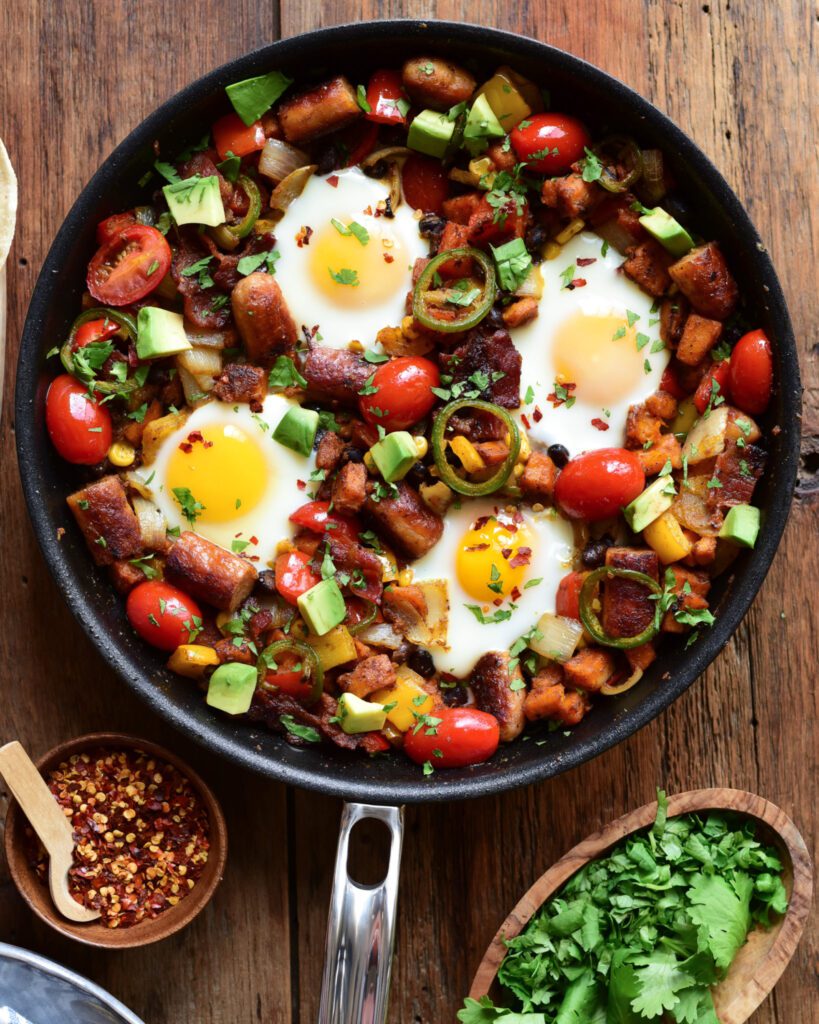 A top down of a skillet hash with four sunny side up eggs and loaded with potatoes and veggies.