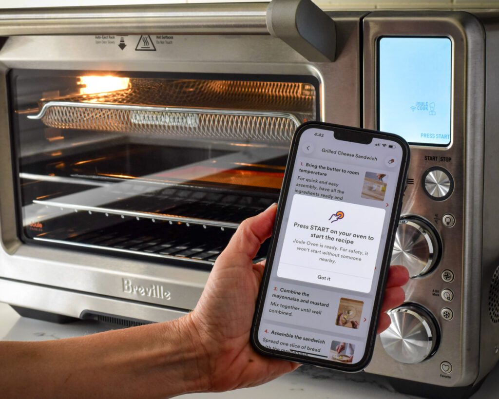 Someone holding an iPhone in front of an air fryer with the air fryer app turned on.