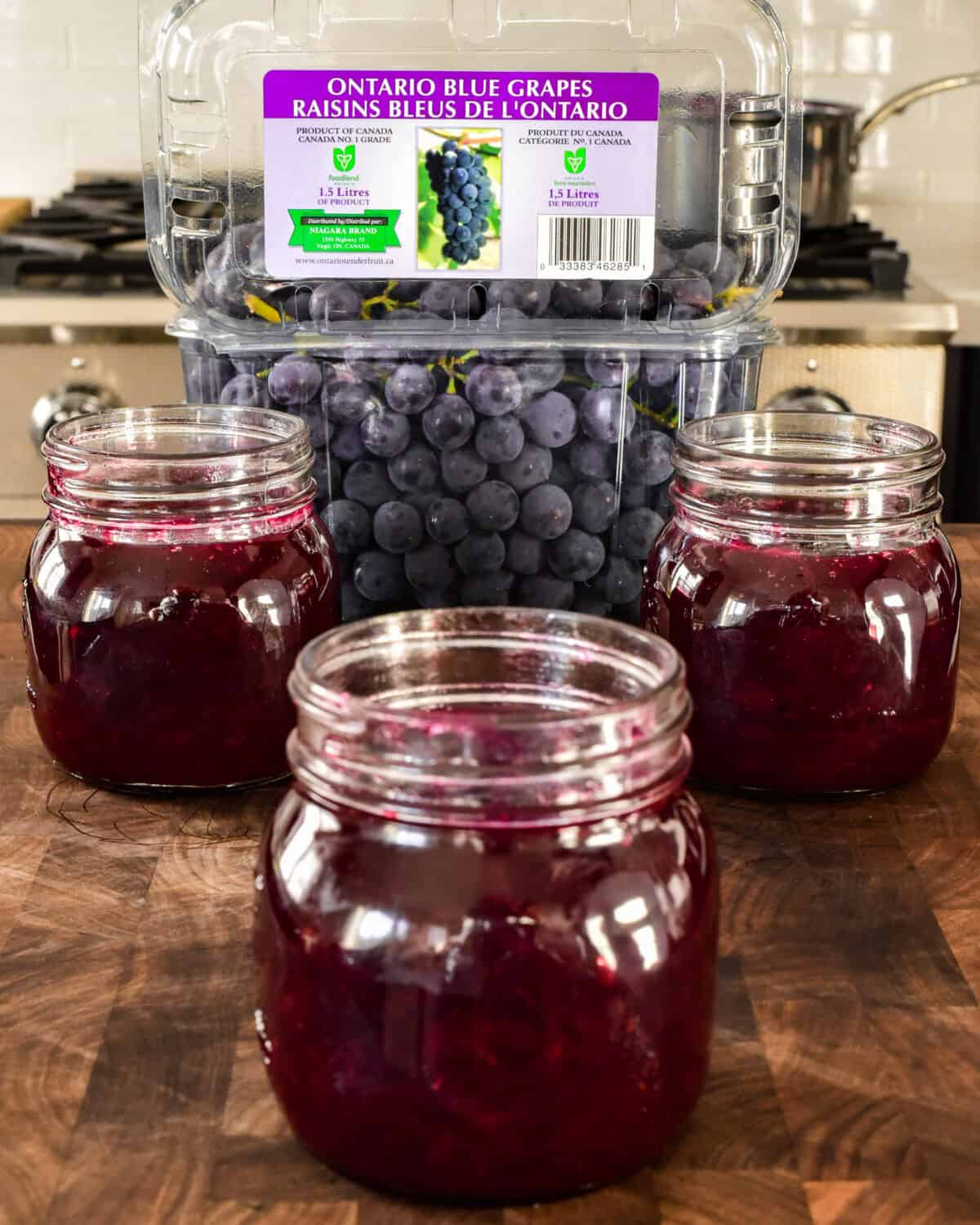 Three jars of jam in front of a container of Coronation grapes