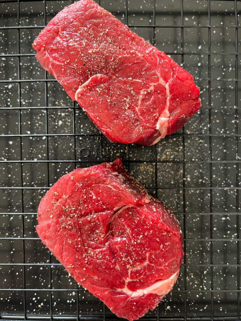 Two seasoned filet mignon steaks on a rack.