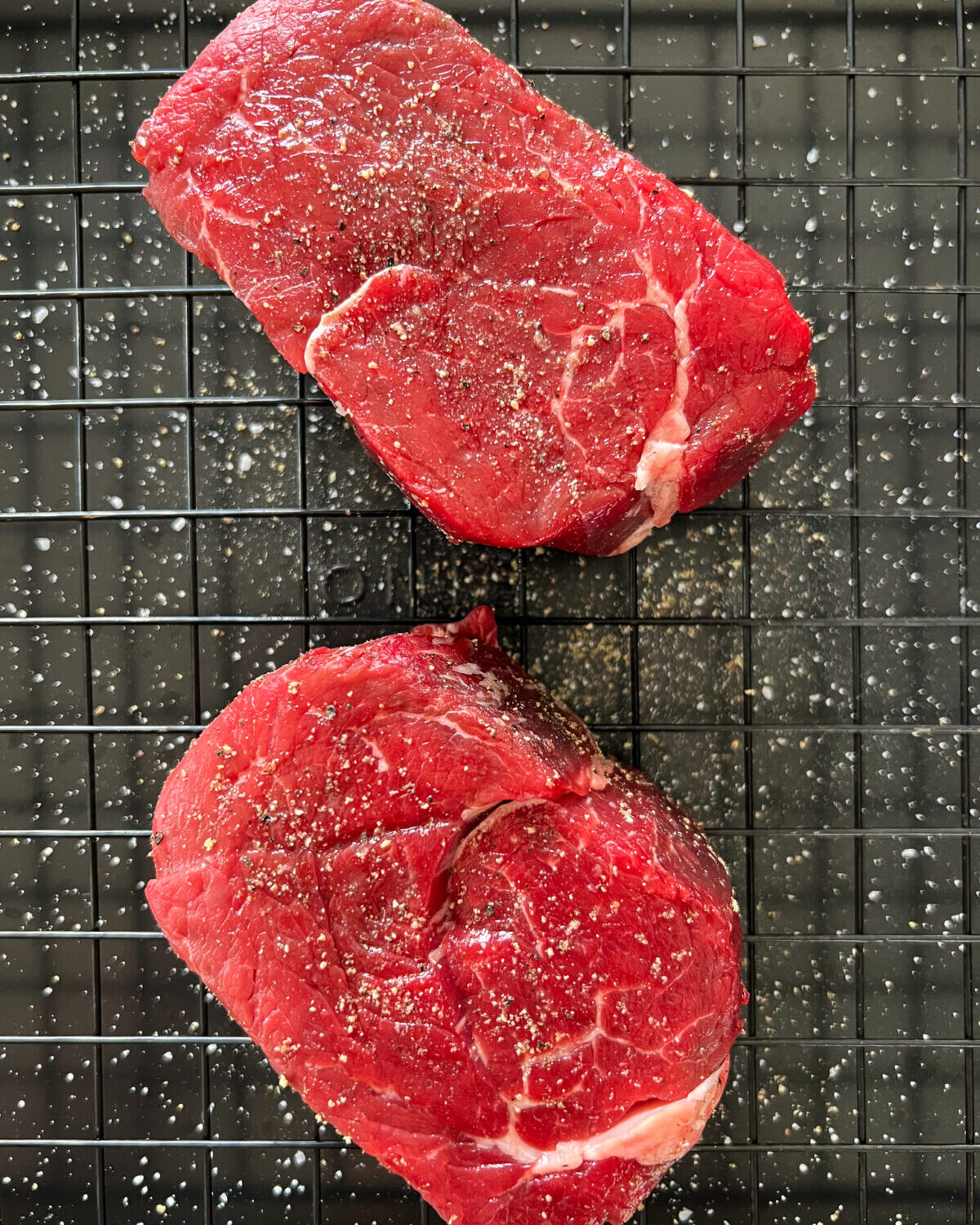 Two seasoned filet mignon steaks on a rack.