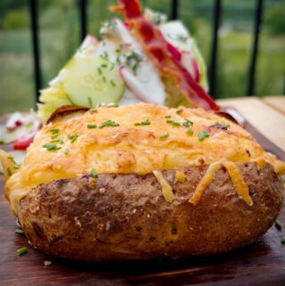 A side view of a baked potato with cheese and chives on the top.