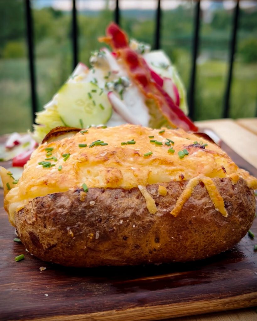 A side view of a baked potato with cheese and chives on the top.
