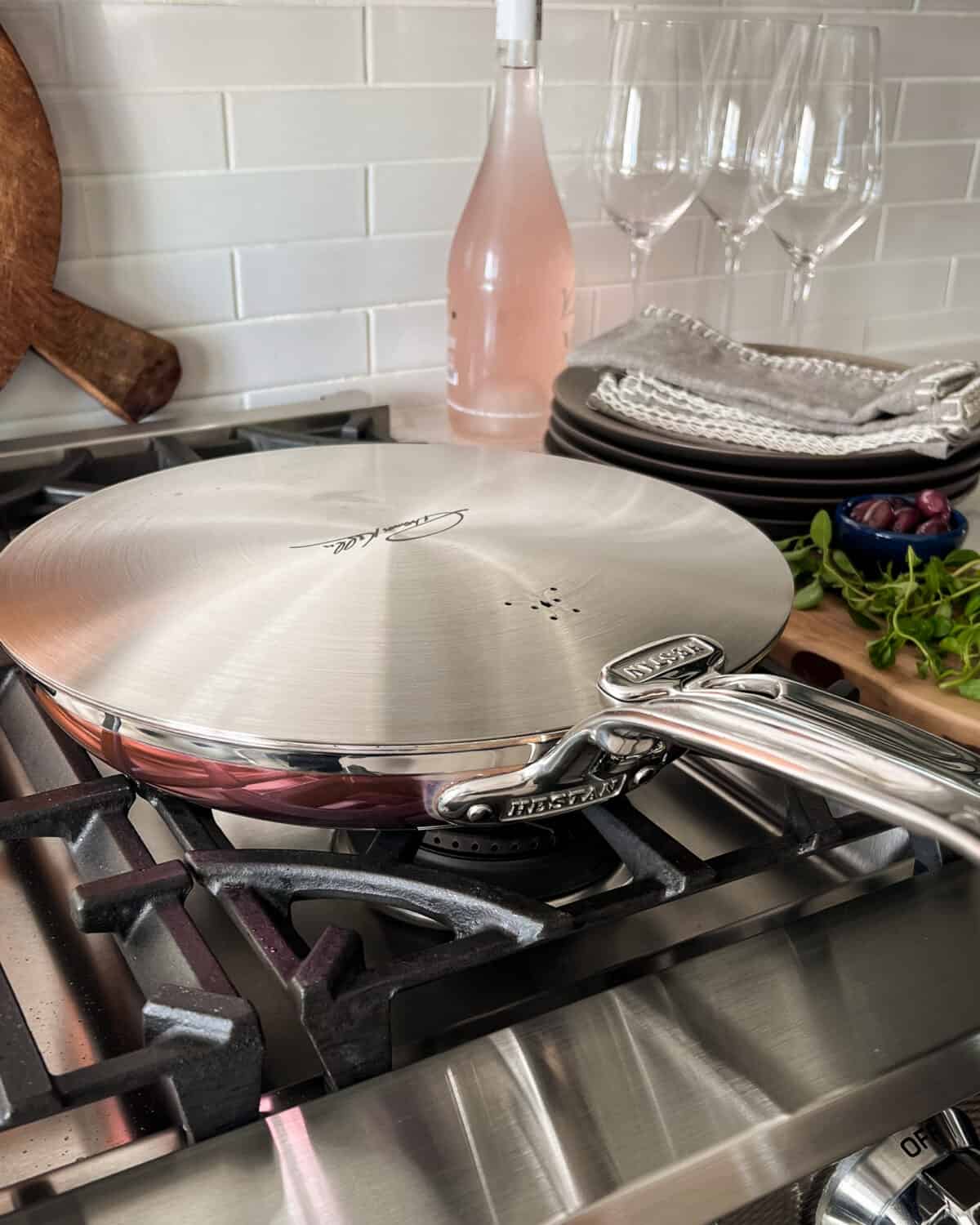 A copper skillet with a lid on a range with rose wine and glasses in the background.