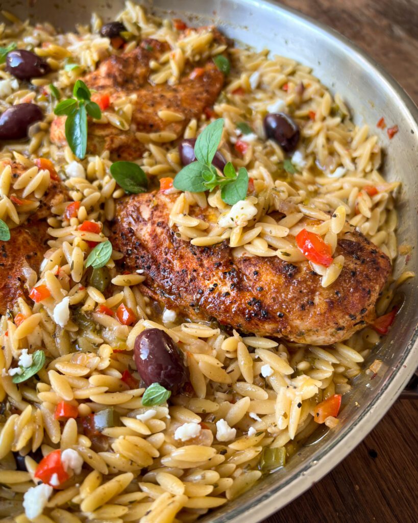 A close up look at an orzo and chicken dish in a skillet.