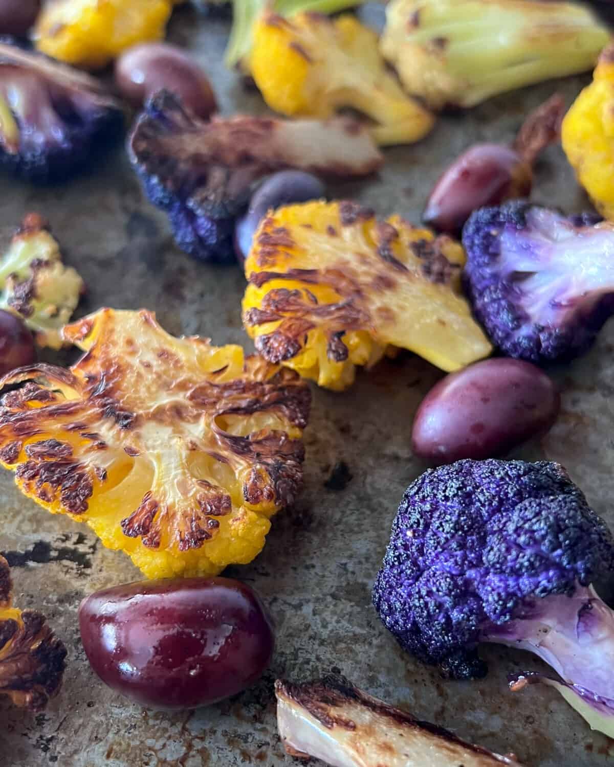 A close up of crispy roasted cauliflower with olives on a sheet pan.