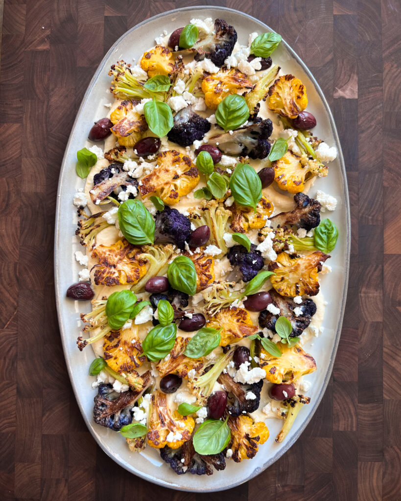 Three varieties of roasted cauliflower and olives on a bed of hummus with basil and feta. 