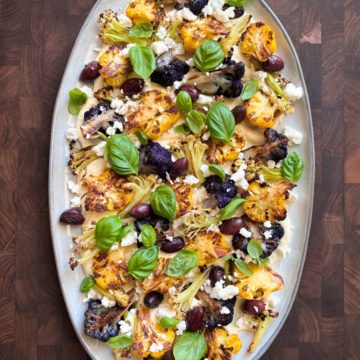 Three varieties of roasted cauliflower and olives on a bed of hummus with basil and feta.