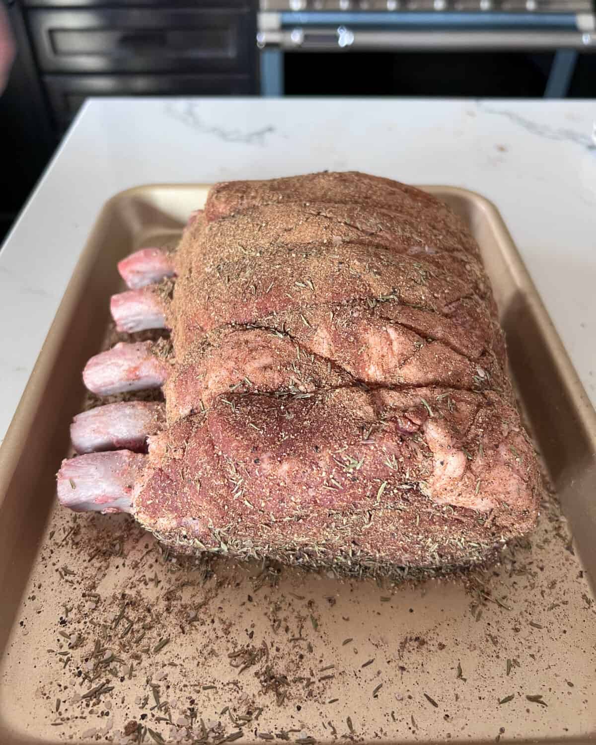 A five bone rack of pork dry rubbed with jerk seasoning in a tray.