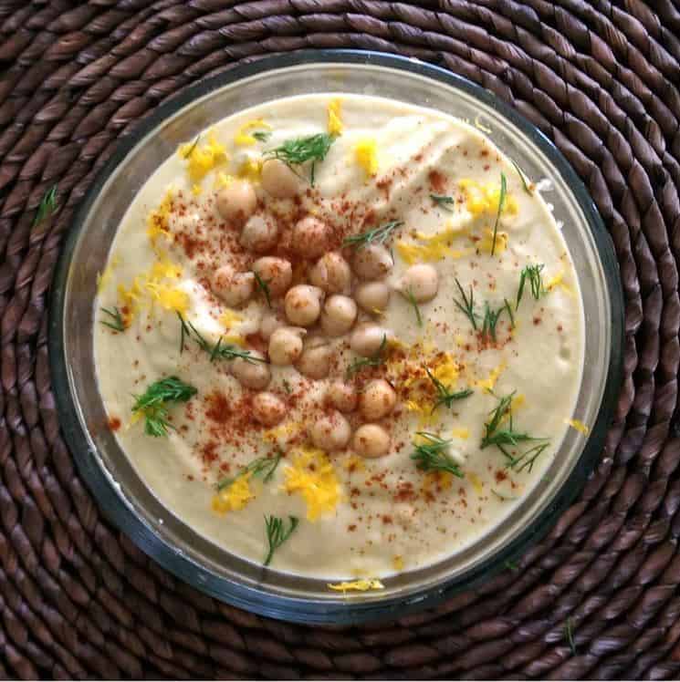 A bowl of hummus, topped with chickpeas, grated lemon, dill and paprika.