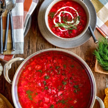 This is a top-down image of a big pot and bowl of borscht topped with a swirl of yogurt and dill on top.