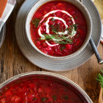 This is a top-down image of a big pot and bowl of borscht topped with a swirl of yogurt and dill on top.