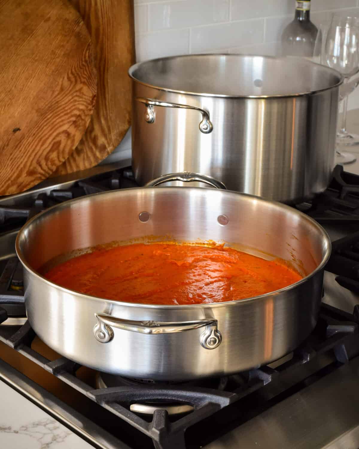 A rondeau and stock pot on the stove with a red sauce in the rondeau.