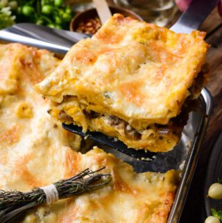 A piece of Butternut Squash and Turkey Sausage Lasagna is being lifted out of a baking pan.