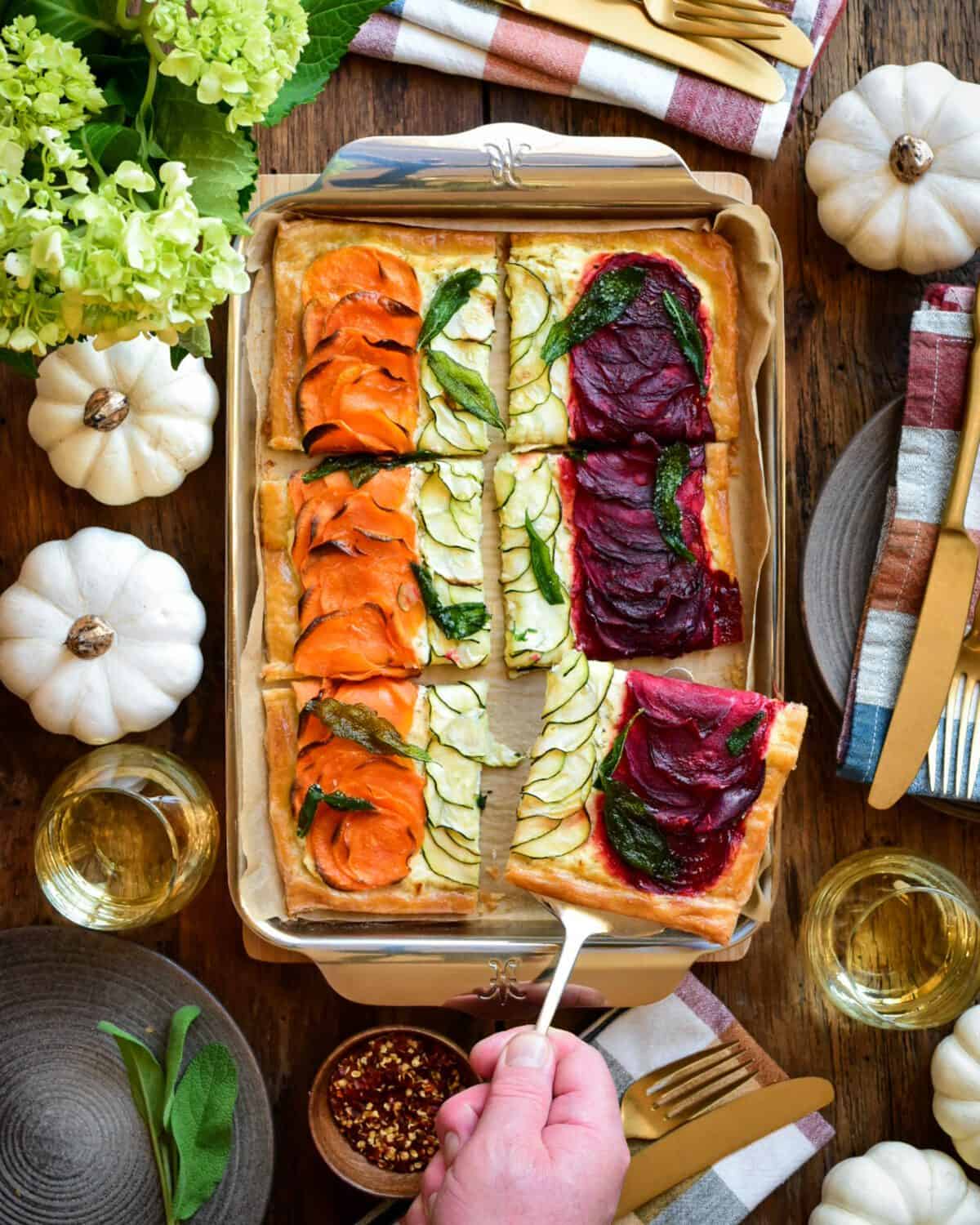 A puff pastry with three rows of root vegetables, The tart is cut in six pieces. The table setting is a fall theme.