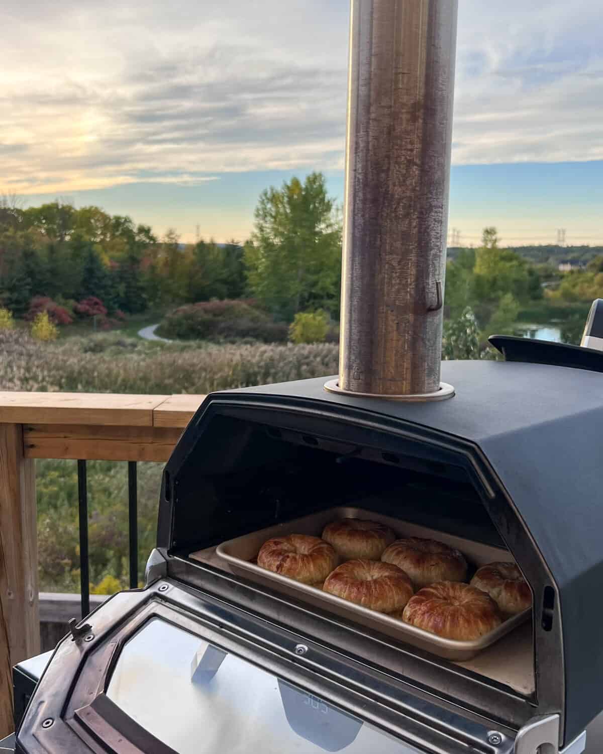 A pan of 6 Savoury Apple-Brie Hand Pies in an Ooni oven with a sunset and trees in the background.