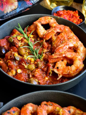A bowl with six colossal shrimp along one side on a base of spicy sauce.