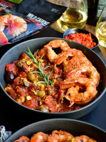 A bowl with six colossal shrimp along one side on a base of spicy sauce.