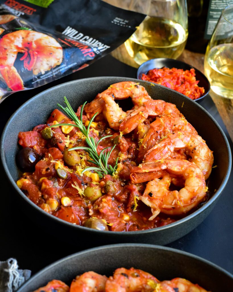 A bowl with six colossal shrimp in a spicy sauce.