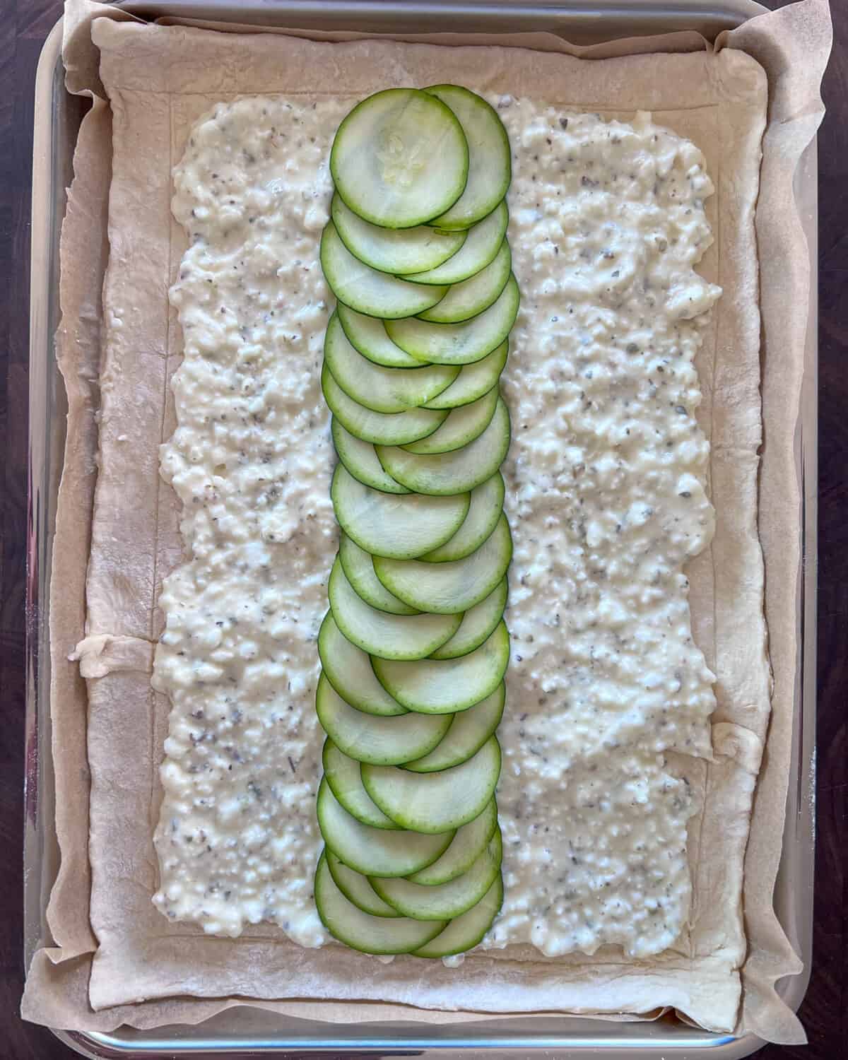 A row of zucchini laid over the cheese layer on the puff pastry.
