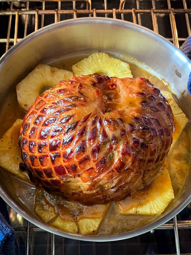 A glazed ham sitting on pineapple slices is coming out of the oven.