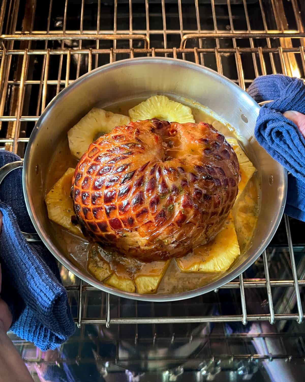 A glazed ham sitting on pineapple slices coming out of the oven.