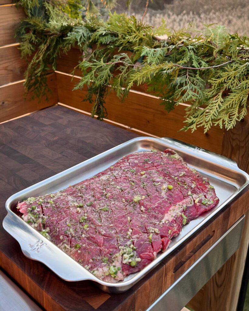 A marinated and crosshatched steak in a sheet pan ready to be grilled.