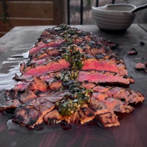 A medium rare and sliced grilled flank steak with herb sauce over the top.