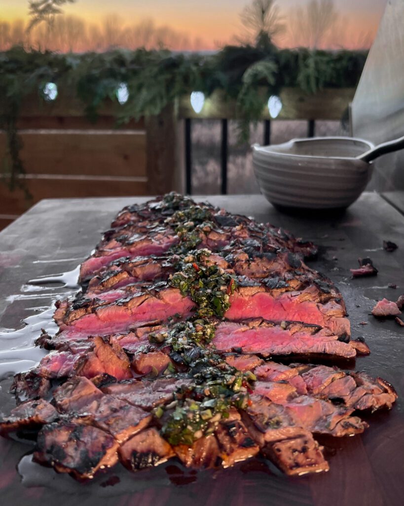 A medium rare and sliced grilled flank steak with herb sauce over the top.