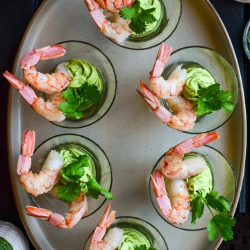 Six individual shrimp cocktails in glass cups with avocado crema.