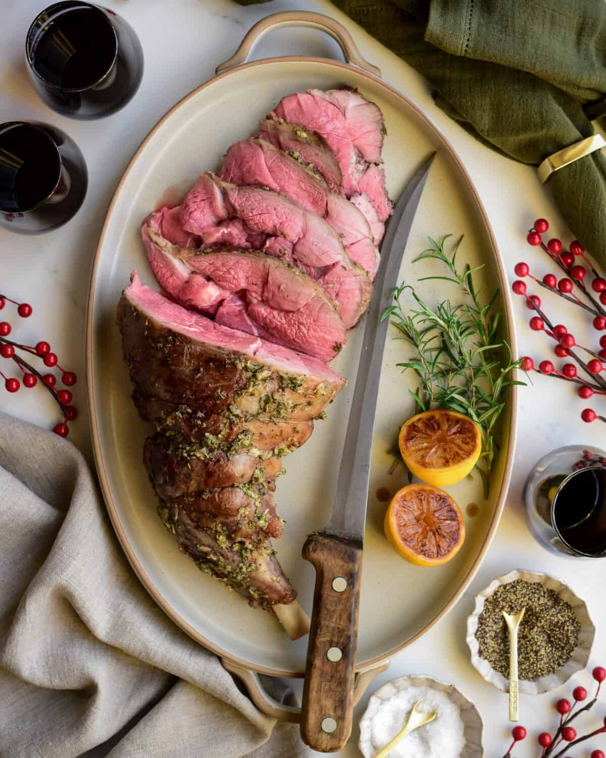 A medium rare Roasted Leg of Lamb with Lemon Vinaigrette half sliced on a platter with a knife.