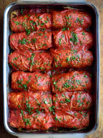 Two rows of cabbage rolls with tomato sauce in a baking pan.