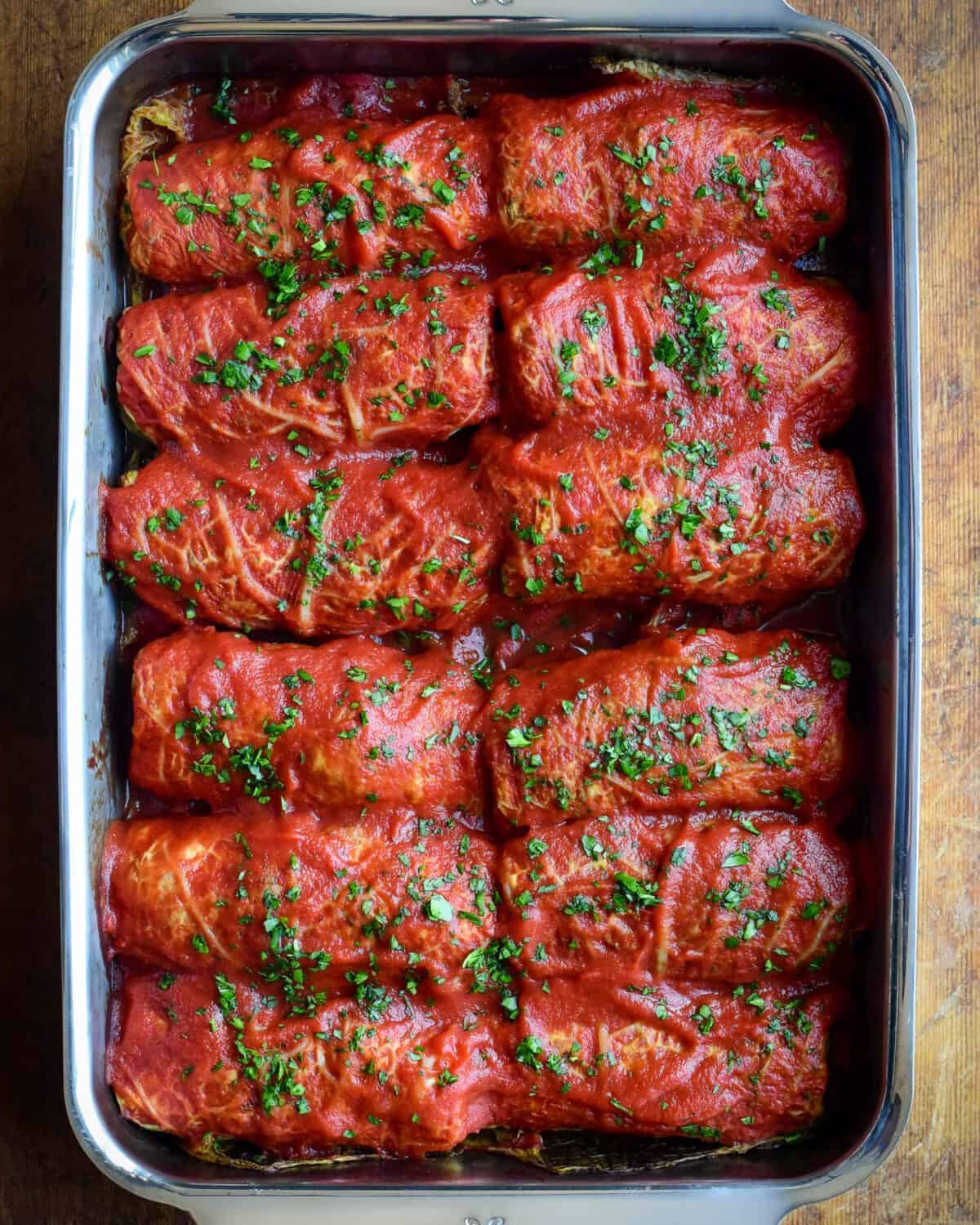 Two rows of cabbage rolls with tomato sauce in a baking pan.