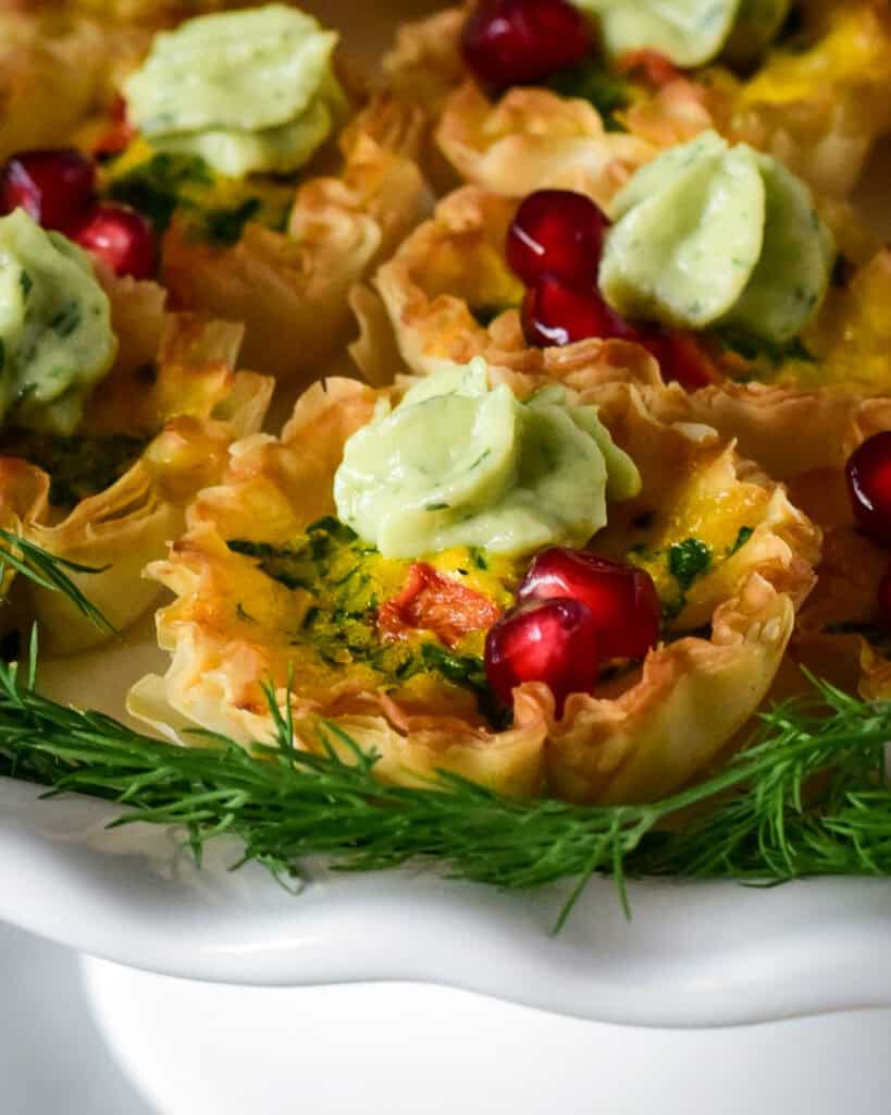 A close up of a festive mini quiche with a crema dollop and arils.