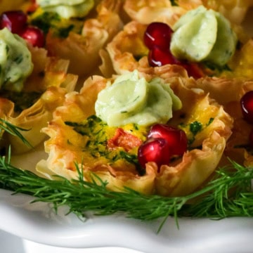 A close up of a festive mini quiche with a crema dollop and arils.