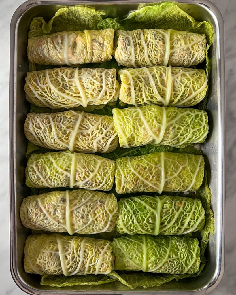 Twelve Savoy cabbage rolls lined up in a pan ready to get sauced and baked.