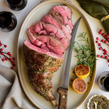 A medium rare Roasted Leg of Lamb with Lemon Vinaigrette half half-sliced on a platter with a knife.