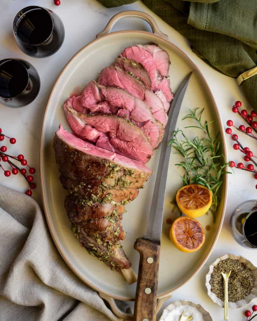 A medium rare Roasted Leg of Lamb with Lemon Vinaigrette half half-sliced on a platter with a knife.