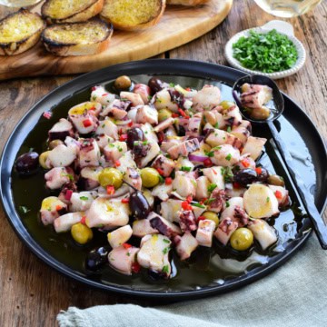 A Marinated Squid Salad with red peppers and olives served with toast and white wine.