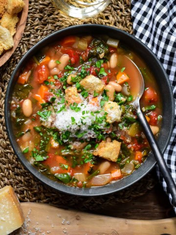 A bowl of rustic vegetable soup with beans, spinach and served with grated Parmesan cheese.