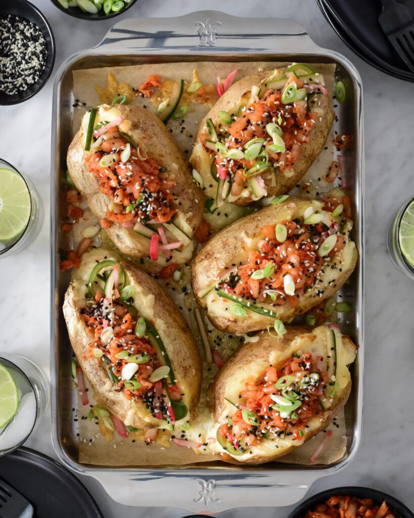 Five Twice-Baked Potatoes topped with Kimchi and pickled veggies on a sheet pan. 